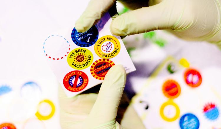 A UCSF School of Nursing volunteer peels a sticker while administering COVID-19 vaccines to children at UCSF Benioff Children's Hospital Oakland. (Photo by Noah Berger)