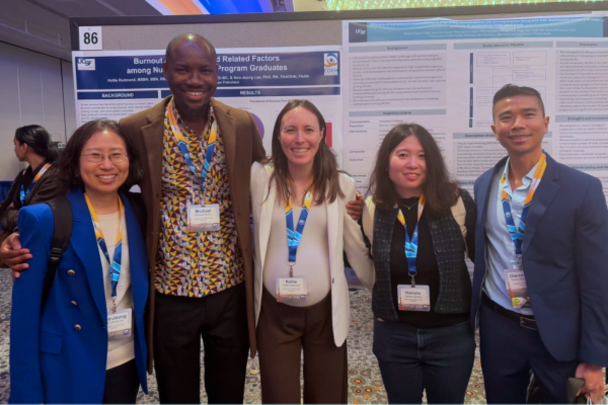 Two men and three women pose in a line together in front of a set of scientific posters. 