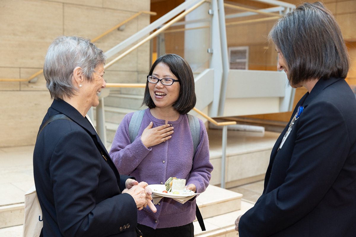 Three people standing together and laughing in an atrium