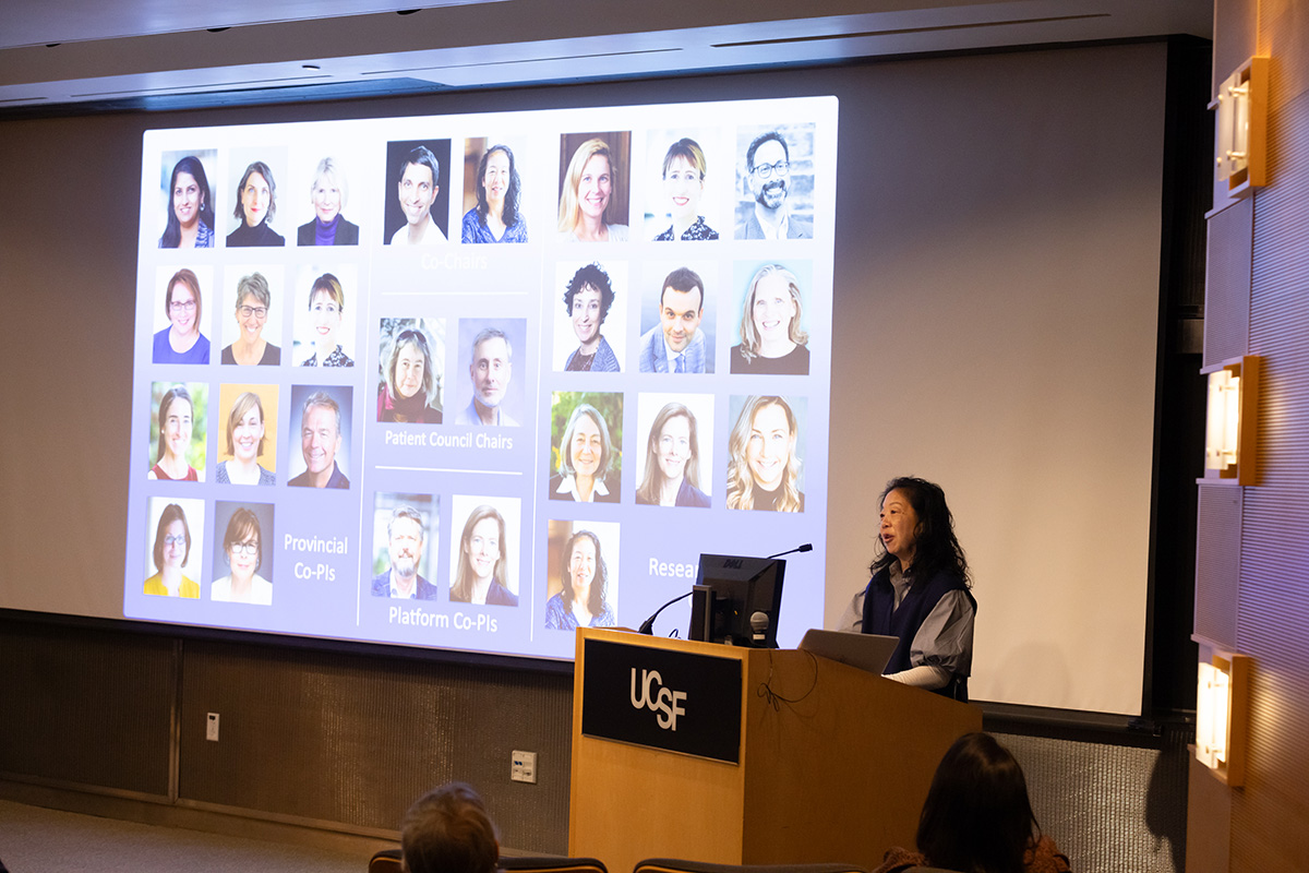 Sabrina Wong speaks from behind a podium with a slide featuring about 30 portraits of colleagues projected next to her.