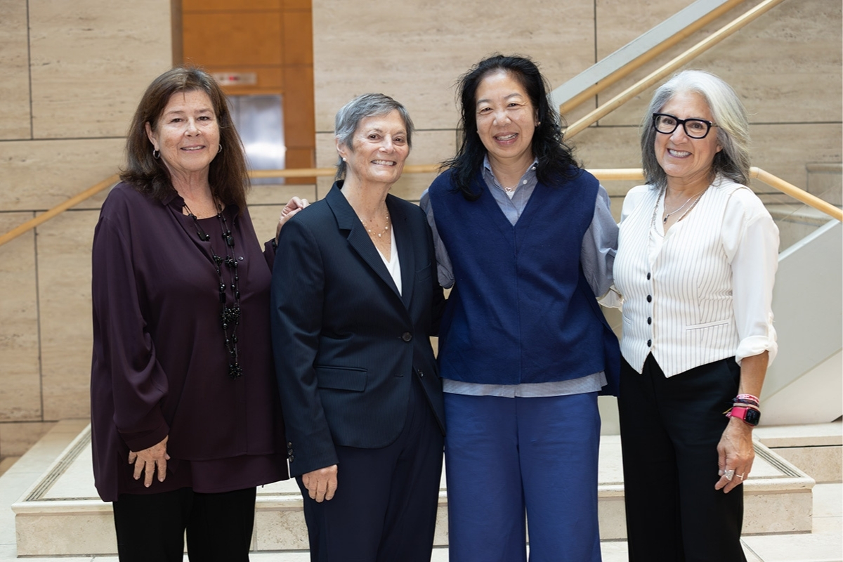 Four women stand together, smiling. 