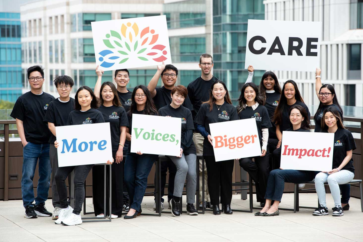 Group of people holding signs that read "CARE: More Voices, Bigger Impact!"