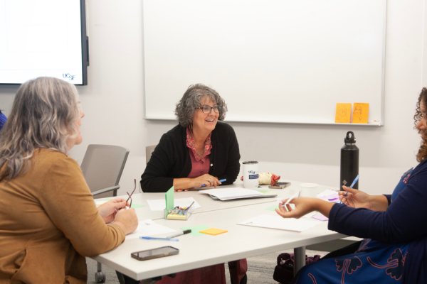 Three faculty members talk at a table.