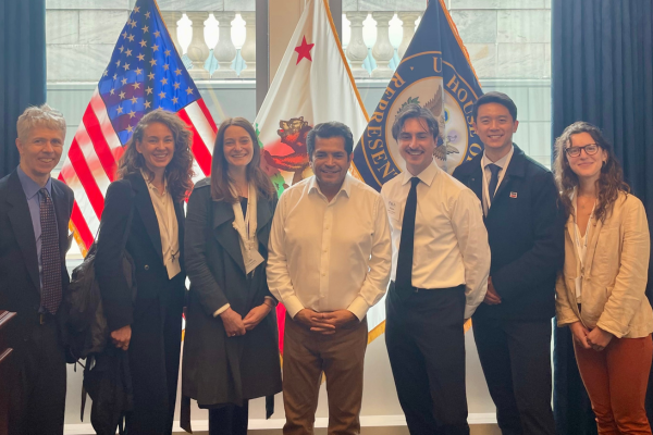 Six people stand in front of flags
