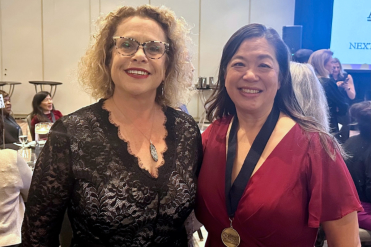 Juli Maxworthy and Angel Kuo pose together in a busy ballroom. Kuo is wearing a medal around her neck. 