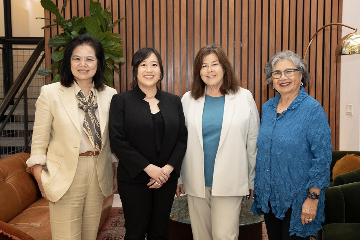 Four women stand together, smiling at the camera. 