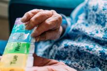 Elderly hands holding a colorful pill organizer.