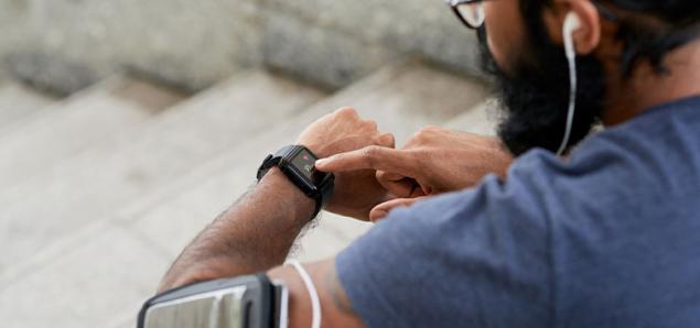 Runner looks at wearable health tracker while exercising.