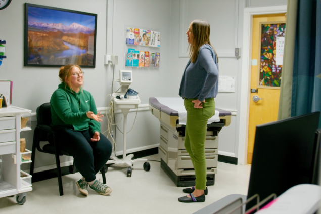 A nurse practitioner speaks to a patient in a clinic room
