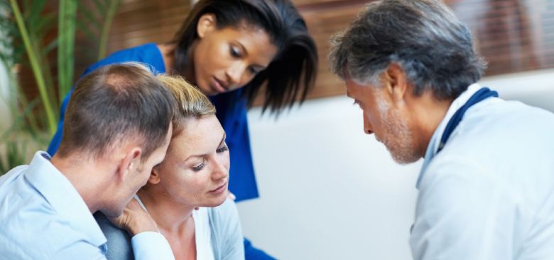 A health care profoessional speaks to a patient while the patient is comforted by two other people.