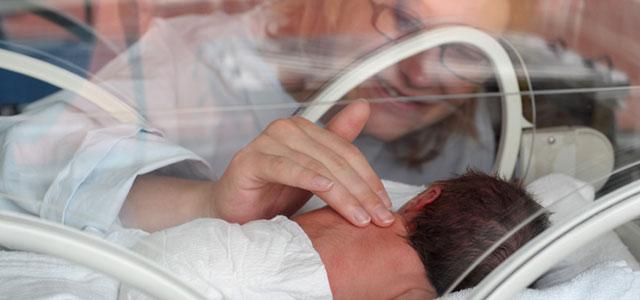 Parent touches newborn in an incubator. 