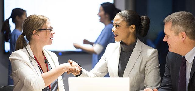 Five people stand in an auditorium while two people shake hands.