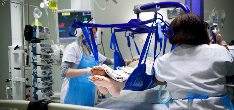  Two nurses move a patient using a lift. 