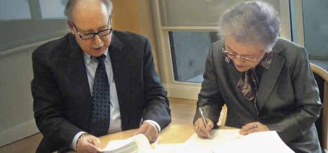 Dean David Vlahov with Hiroko Minami sign papers while seated at a table