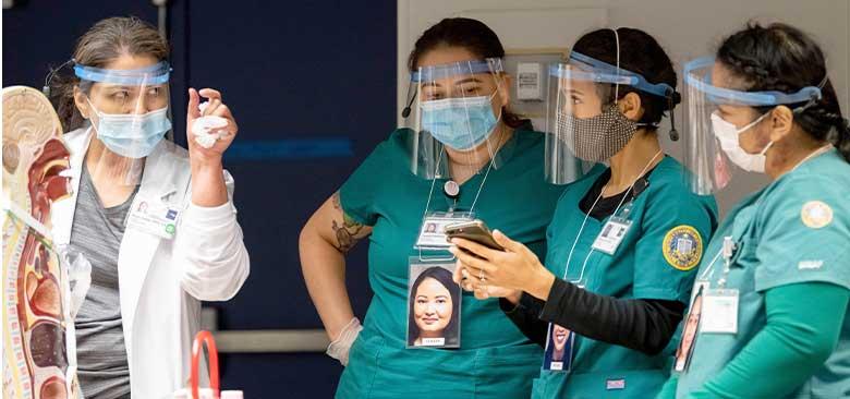 Three UCSF School of Nursing students listen to their instructor during a lab class.