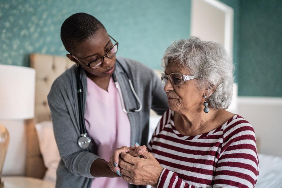 Home health aide supports elderly patient to stand