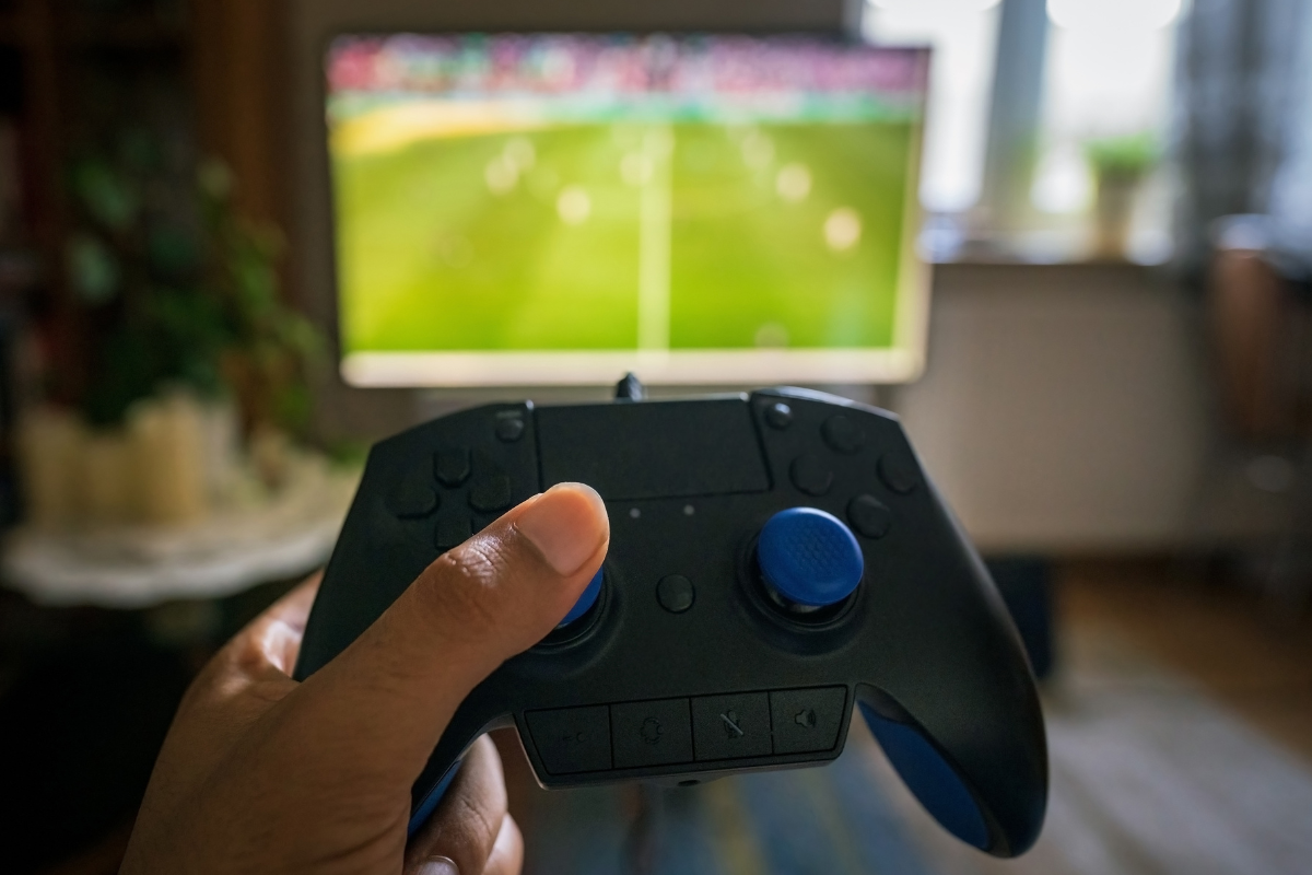 Hand holding video game controller with television in background
