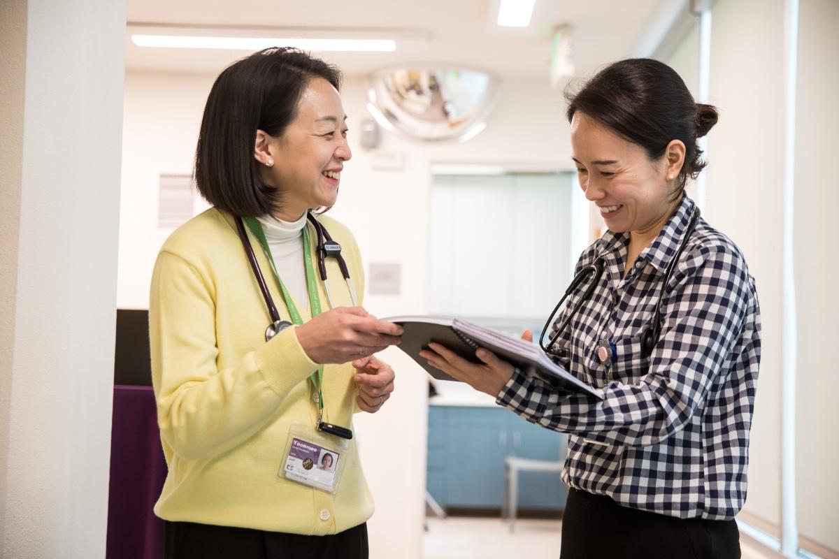 Two nurses consult with one another in the hall of a hospital.