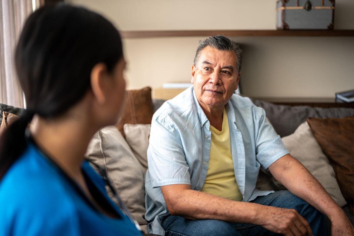 Older patient sits on a couch and speaks to a nurse