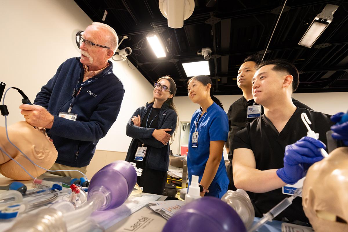 Four students watch as a professor demonstrates a procedure in a simulation lab.