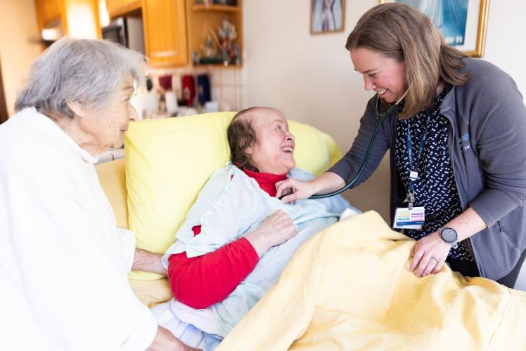 A nurse practitioner provides care to a patient; the patient's mother stands next to patient.