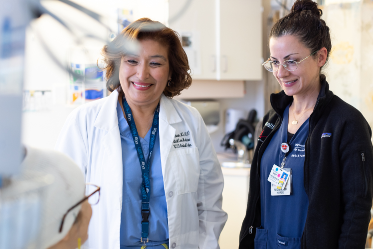 Two nurses speak with a patient in a hospital room.