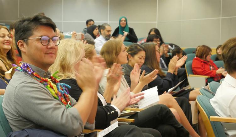 DNP graduate Bryan Chin, seated with peers from his cohort, applauds after colleague Summer Thompson's remarks. 