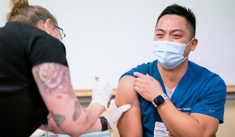 On the first day of COVID-19 vaccinations at UCSF in December 2020, Liesl Piccolo (left), master’s student at the UCSF School of Nursing, administers the Pfizer vaccine to Michael Lejano, UCSF respiratory care practitioner.