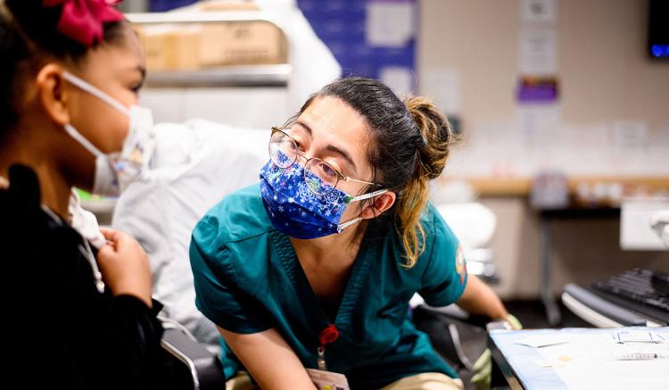 UCSF School of Nursing MEPN student Aby Romero speaks with a patient before administering during a clinic at UCSF Benioff Children's Hospital Oakland on Dec. 11, 2021. (Photo by Noah Berger)y