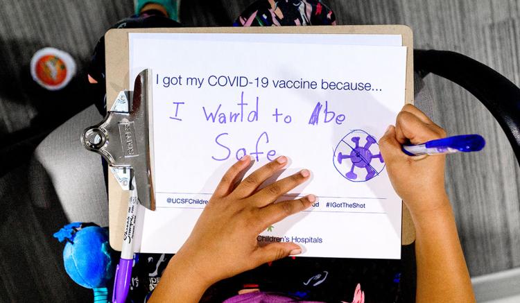 A child writes a note after receiving a COVID-19 vaccine at UCSF Benioff Children's Hospital Oakland on Dec. 11, 2021. (Photo by Noah Berger)