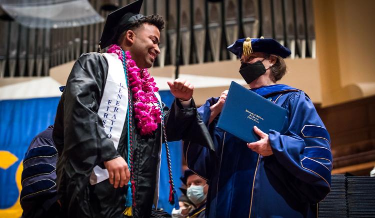 Mykel Bennett, a master's graduate, receives a congratulatory elbow bump from Dean Catherine Gilliss at Commencement.