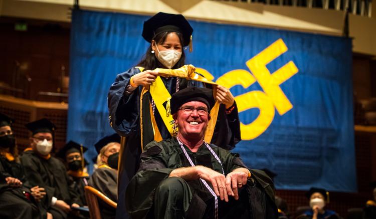 Professor Jyu-Lin Chen places the doctoral hood on graduate Mitchel Erickson at Commencement.