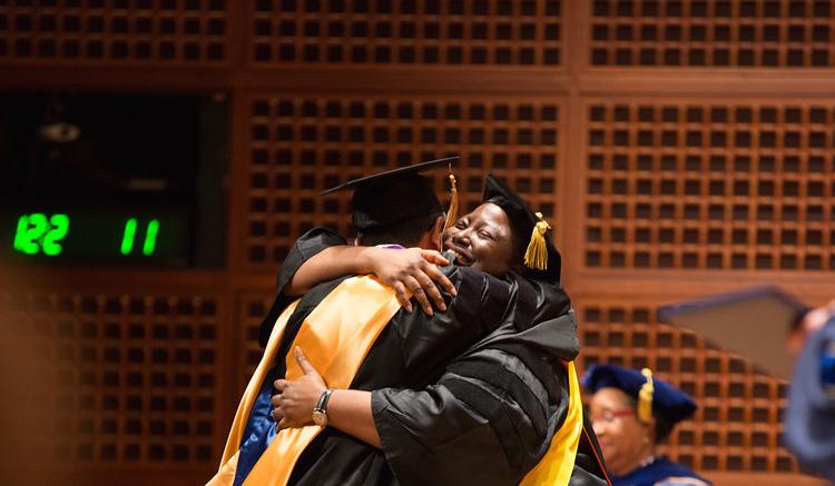 Student and faculty embrace in celebration following a doctoral hooding.