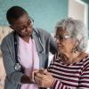 Home health aide supports elderly patient to stand