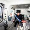 Nurse kneeling in helicopter wearing helmet with microphone, reaching into clear case of supplies. 