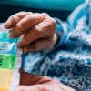 Elderly hands holding a colorful pill organizer.