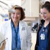 Two nurses smiling down at a patient in a bed. The nurse on the left is wearing a white coat and a UCSF Health lanyard. 