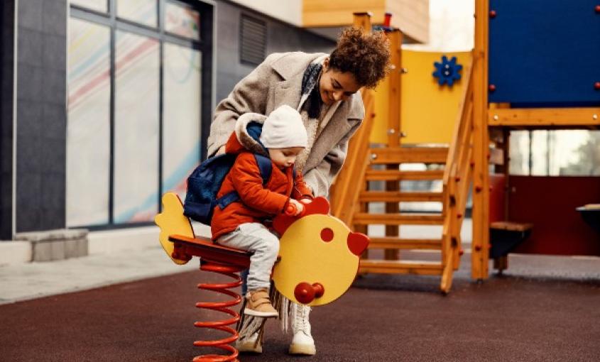 Adult helps child on a playground.