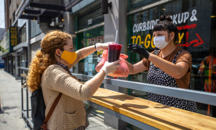 An individual picks up take-out food from a restaurant staff member.