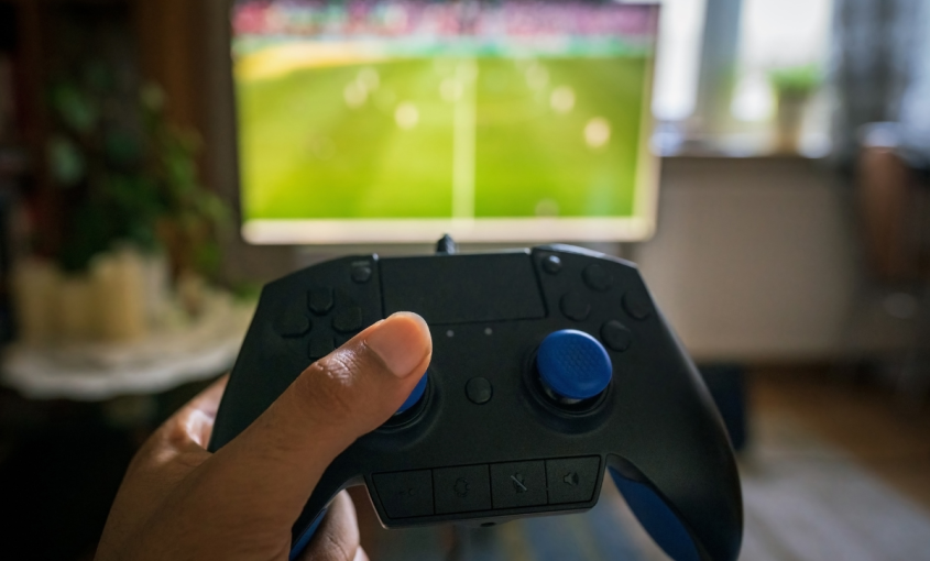 Hand holding video game controller with television in background