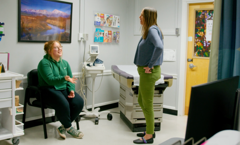 A nurse practitioner speaks to a patient in a clinic room