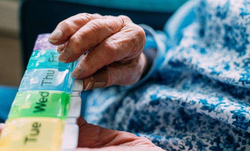 Elderly hands holding a colorful pill organizer.