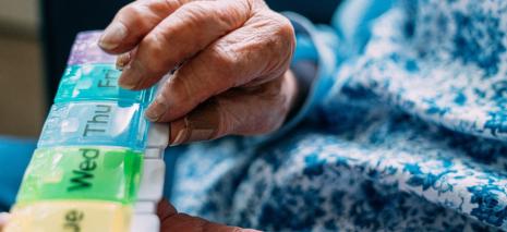 Elderly hands holding a colorful pill organizer.